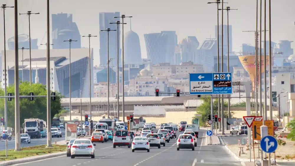 Cars on a Doha highway with bilingual signs for Al Corniche and City Center, West Bay skyline ahead